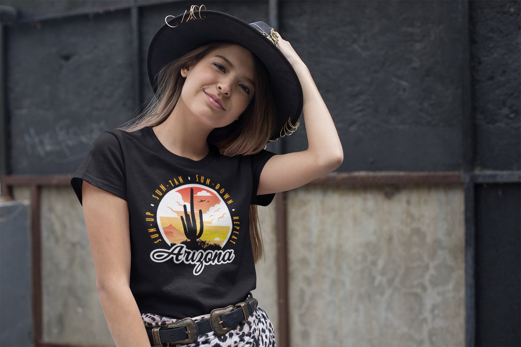 A woman wearing a super soft black t-shirt with an Arizona Sunset Design with the saying Sun Up, Sun Tan, Sun Down, Repeat 