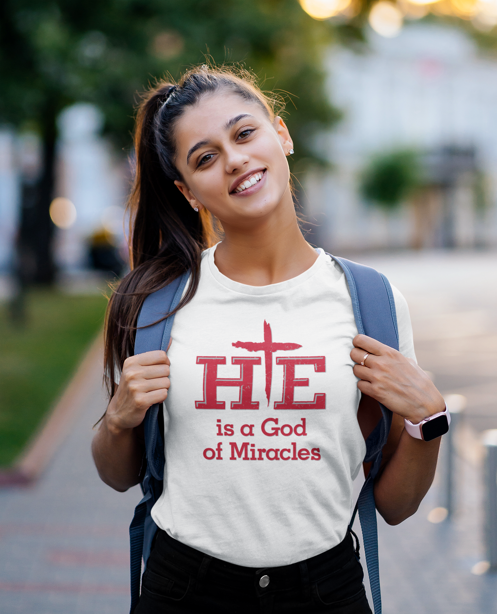 Young woman wearing a white t-shirt with the saying HE is a God of Miracles